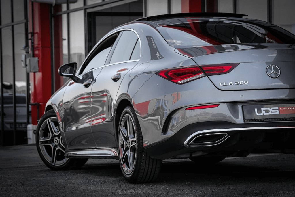 Vista trasera de un automóvil Mercedes CLA 200 plateado en una exhibición, resaltando el diseño aerodinámico y los detalles de sus luces traseras.